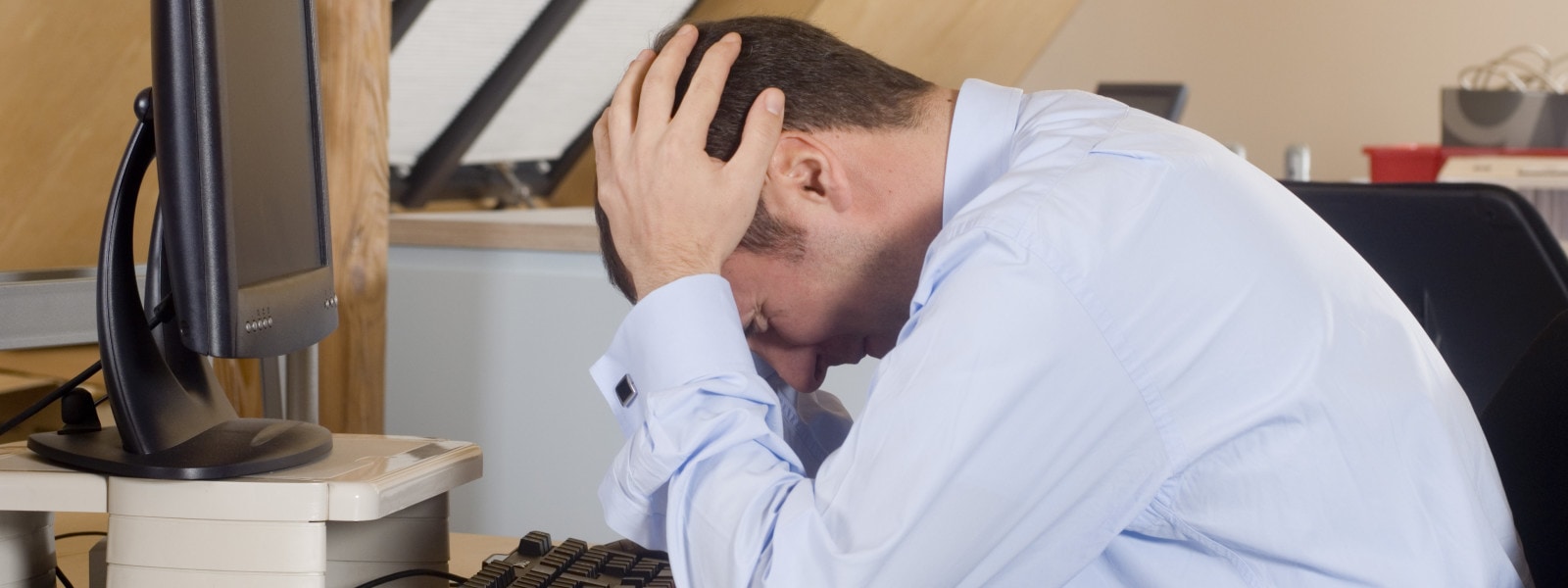 Businessman with his head in his hands sitting in front of a desktop PC