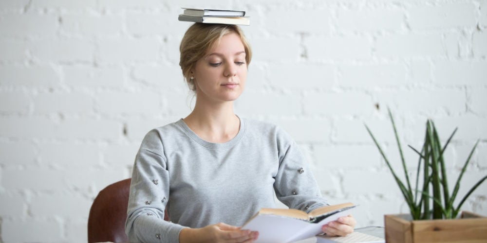 Portrait of attractive woman at desk, books on her head