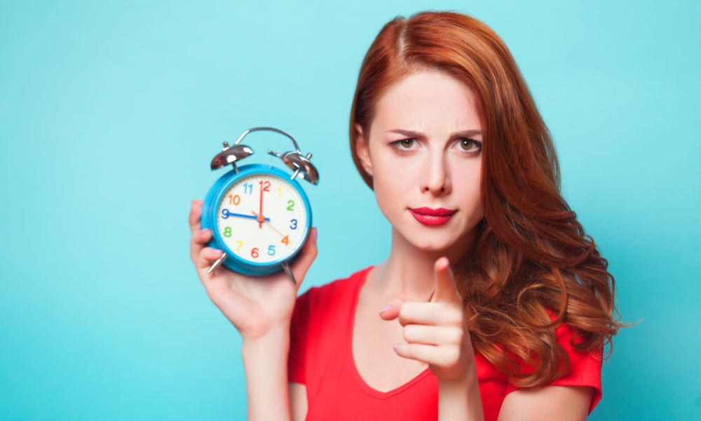 Redhead girl with alarm clock on blue background.